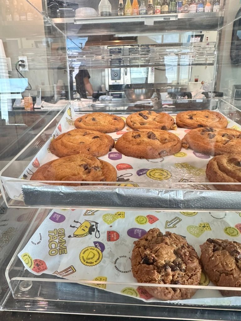 Bakery display case with chocolate chip cookies on trays and café reflections behind glass