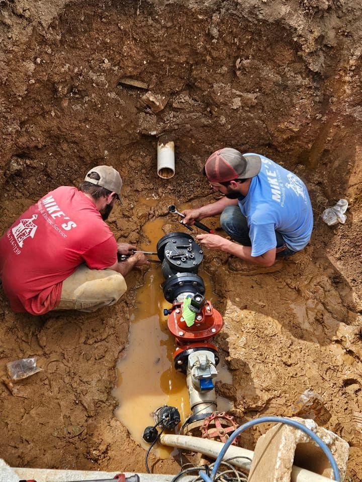 Two men are working on a pipe in the dirt.