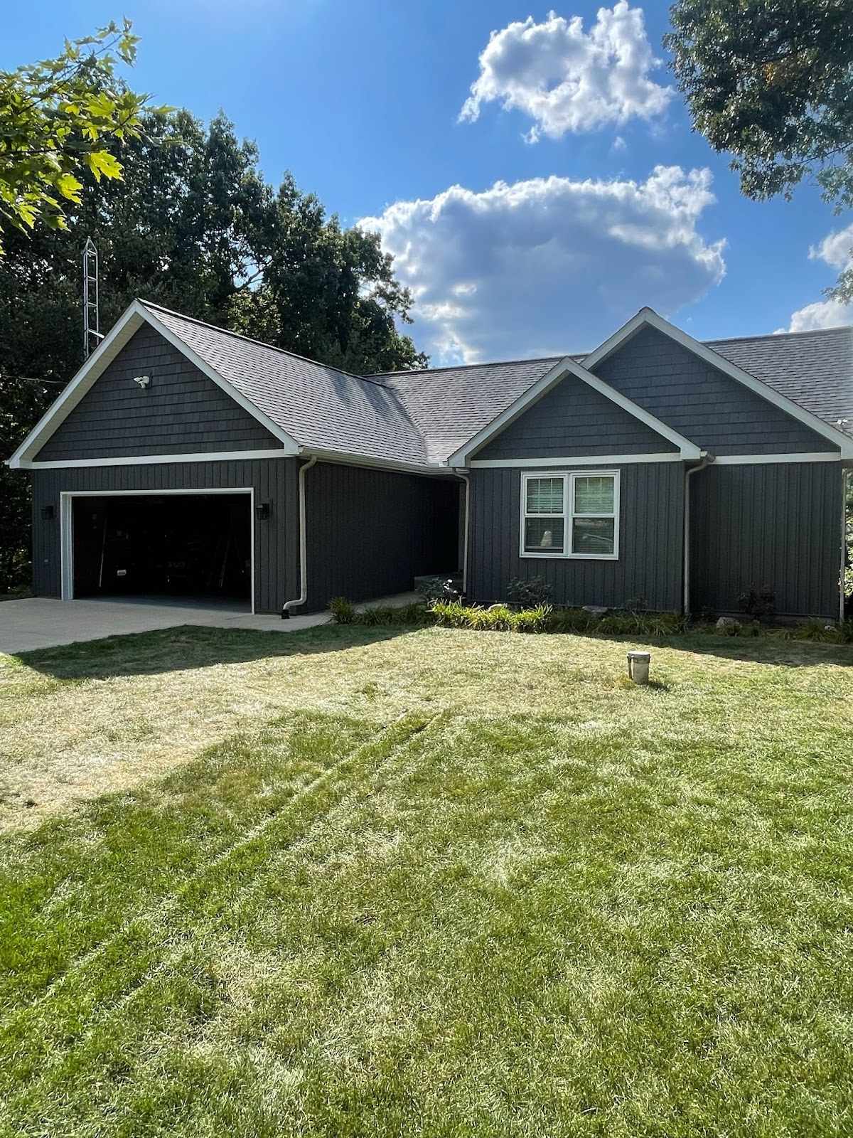 Dark gray house with garage, green lawn, and blue sky with clouds.