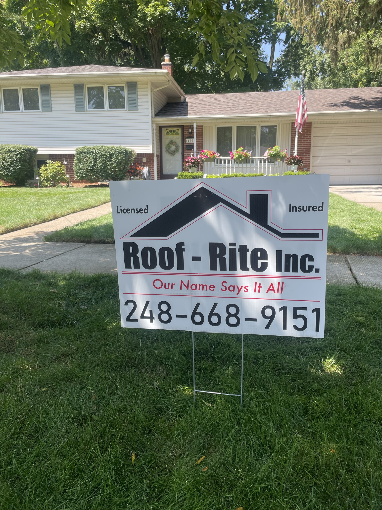 A sign for Roof-Rite Inc. sits in front of a white house with a green lawn.
