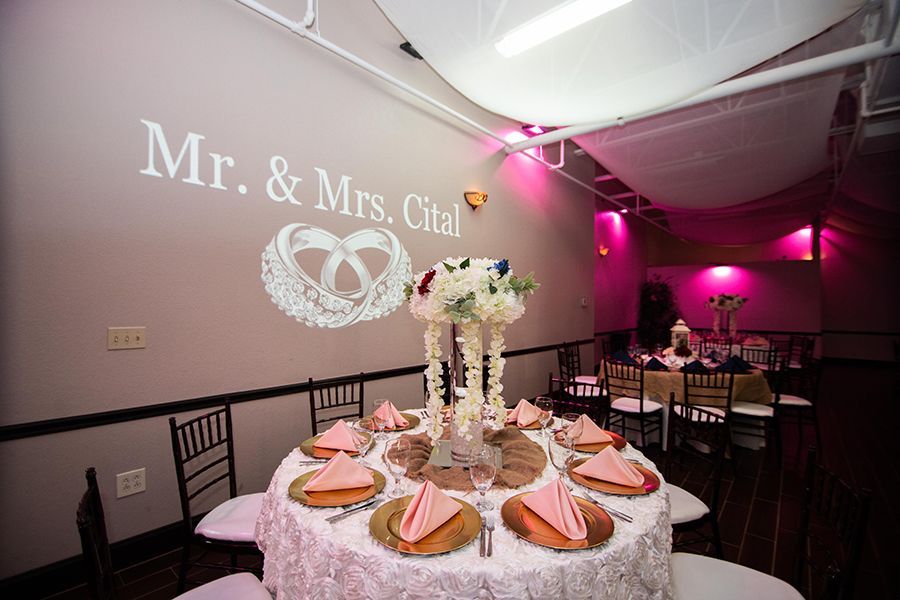 Wedding reception with floral centerpieces, decorated tables, and projected text 
