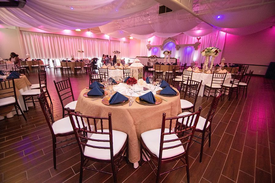 Banquet hall with round tables set for a celebration, draped ceilings, and dark wooden chairs.