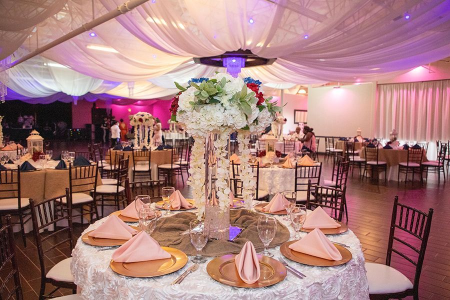 Wedding reception with round tables, floral centerpieces, draping fabric ceiling, and pink and purple lighting.