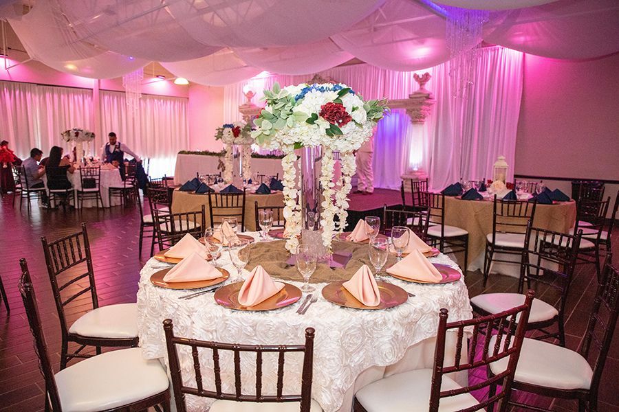 Wedding reception: decorated tables with floral centerpieces, pink lighting, and guests seated.