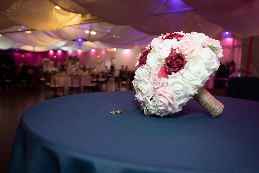 Wedding bouquet with rings on blue tablecloth, blurred reception background.