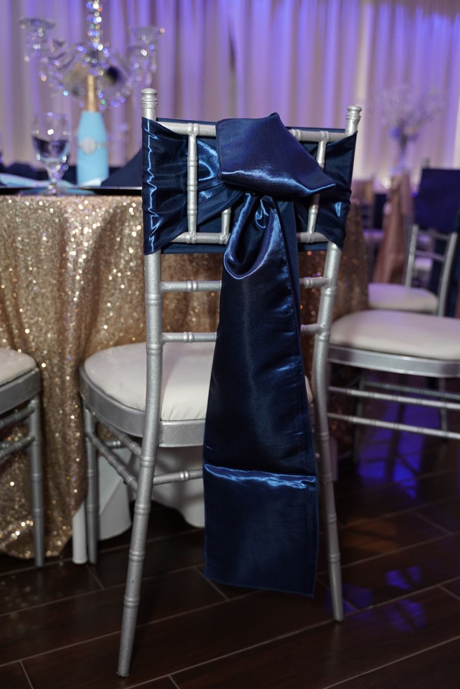 Silver chair with a navy blue satin sash and bow in a decorated room.
