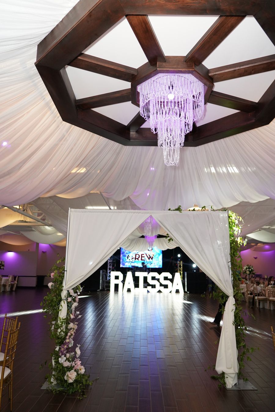 Formal event hall with white draping, chandelier, illuminated name 