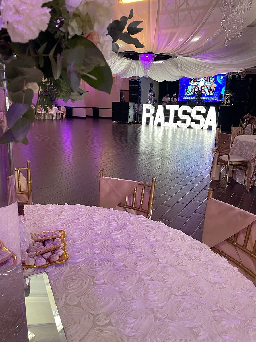 Reception hall decorated for an event, with white floral table setting, dance floor, and a name sign reading 