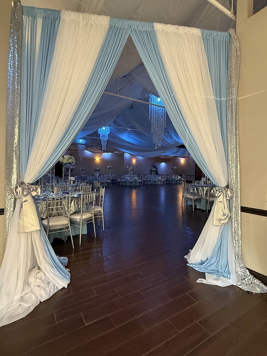 Entrance to a decorated event hall with blue and white draping, tables, and chairs.