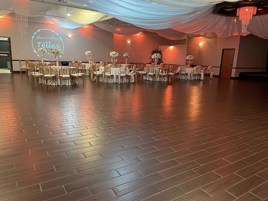 Empty event hall with tables, chairs, and decorations. Wooden floor reflects ceiling lights.