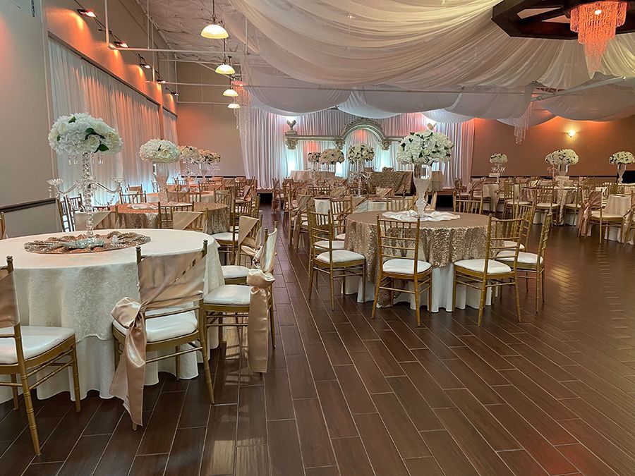 Elegant banquet hall set up for an event, featuring round tables with gold chairs, floral centerpieces, and draping fabric.