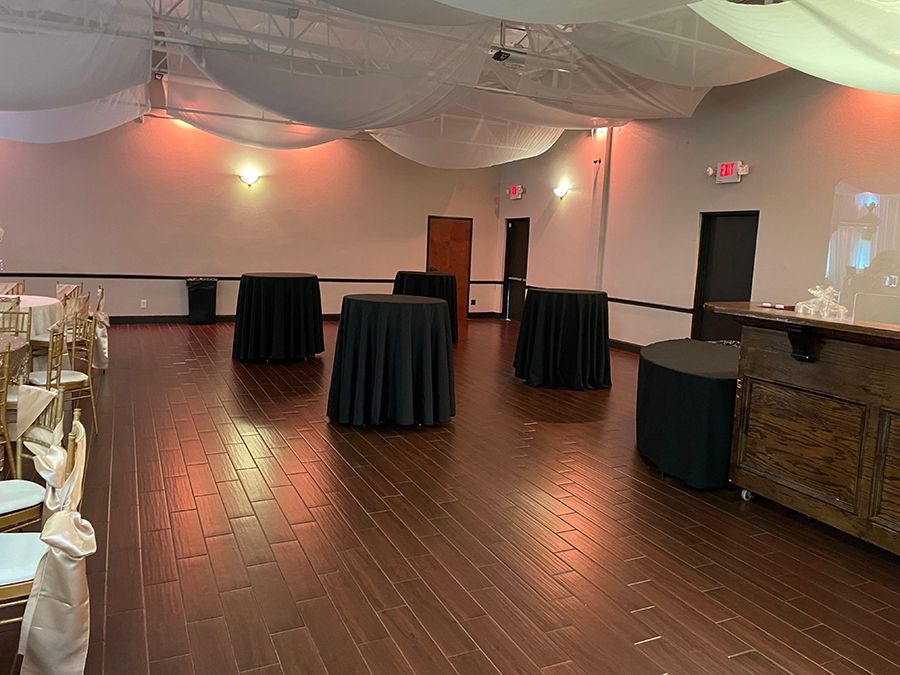 Empty event space with dark wood floor, round black tables, and draped ceiling.