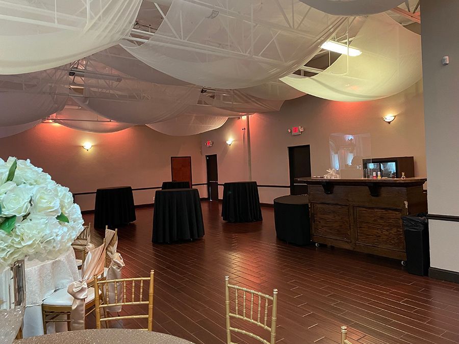 Empty event space with draped ceiling, round tables with black cloths, and a wooden bar.