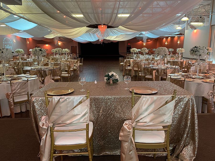 Wedding reception hall with decorated tables, golden chairs, and draped ceiling.