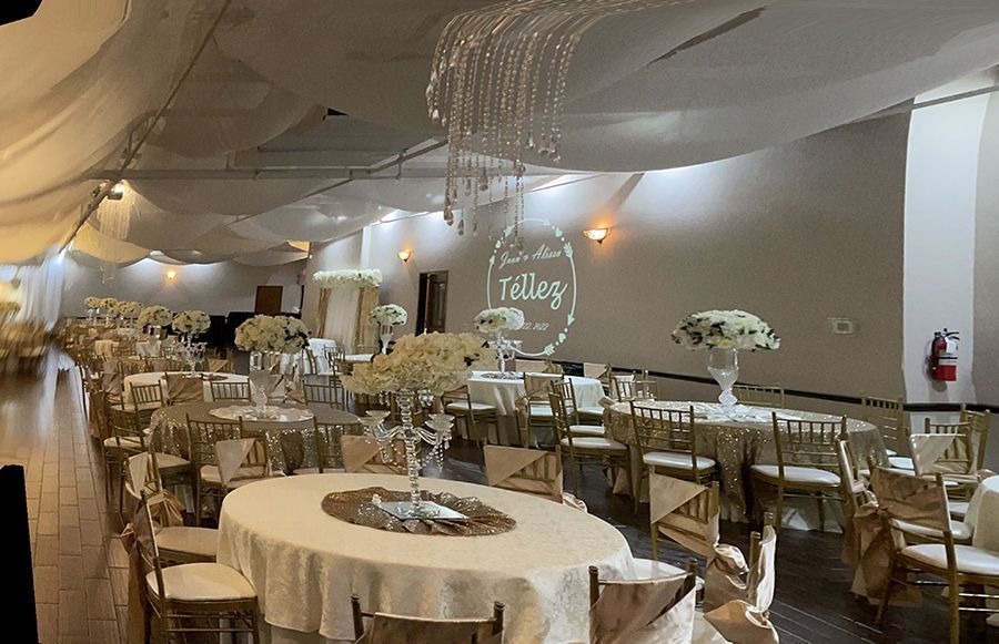 Elegant ballroom set for an event; round tables with gold chairs, floral centerpieces, white draping and projected logo.
