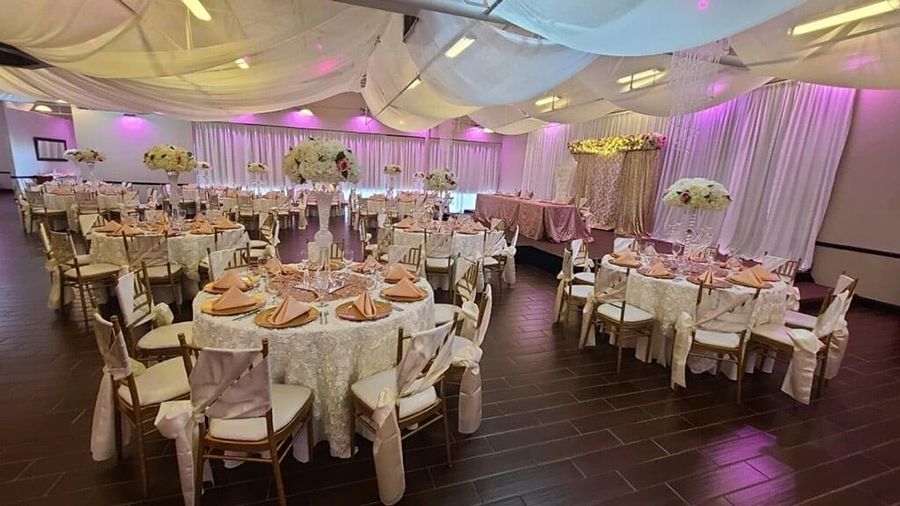 Wedding reception hall with round tables, decorated with pink and white accents. White draped ceiling.