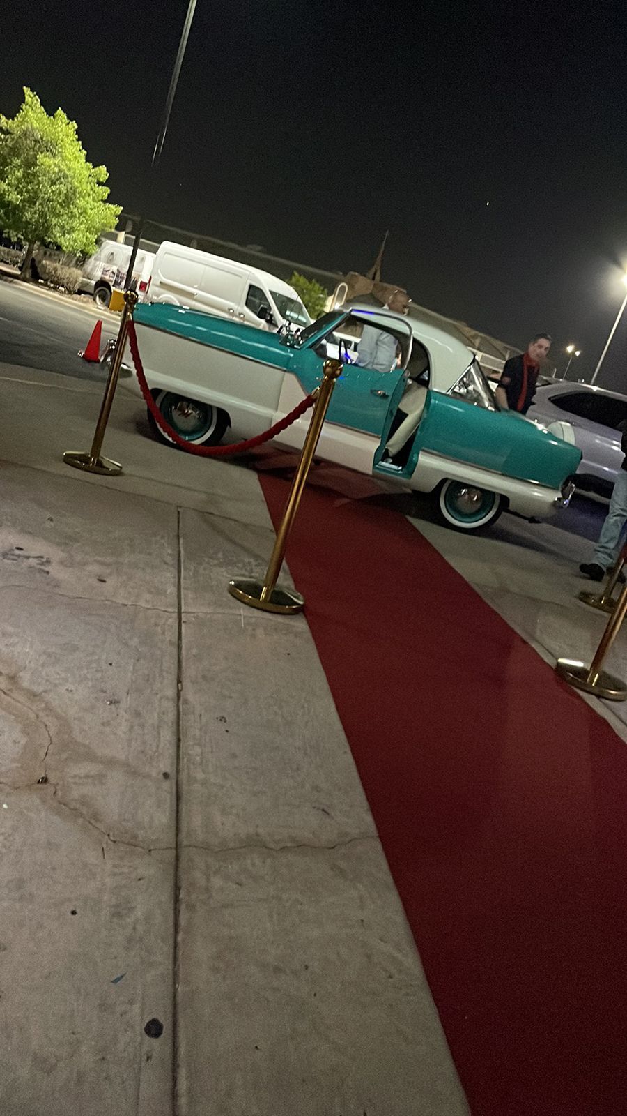 A teal and white vintage car parked on a red carpet at night.