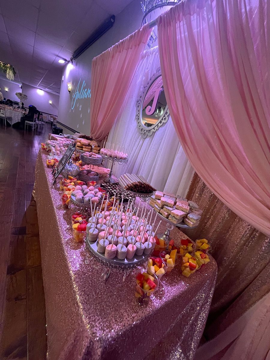 Dessert table at event; pink sequined tablecloth, treats, pink drapes, and a decorative mirror with the letter “A.”