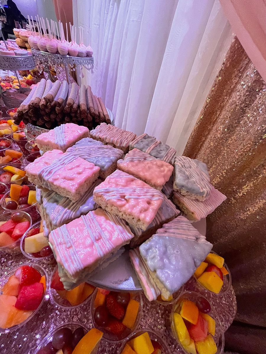 Dessert table with frosted pastel-colored treats, surrounded by fruit cups and other sweets.