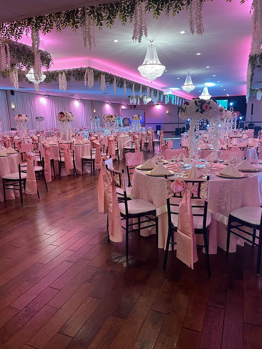 Elegant ballroom set for an event with pink and white decor. Tables are set, and chandeliers hang from the ceiling.
