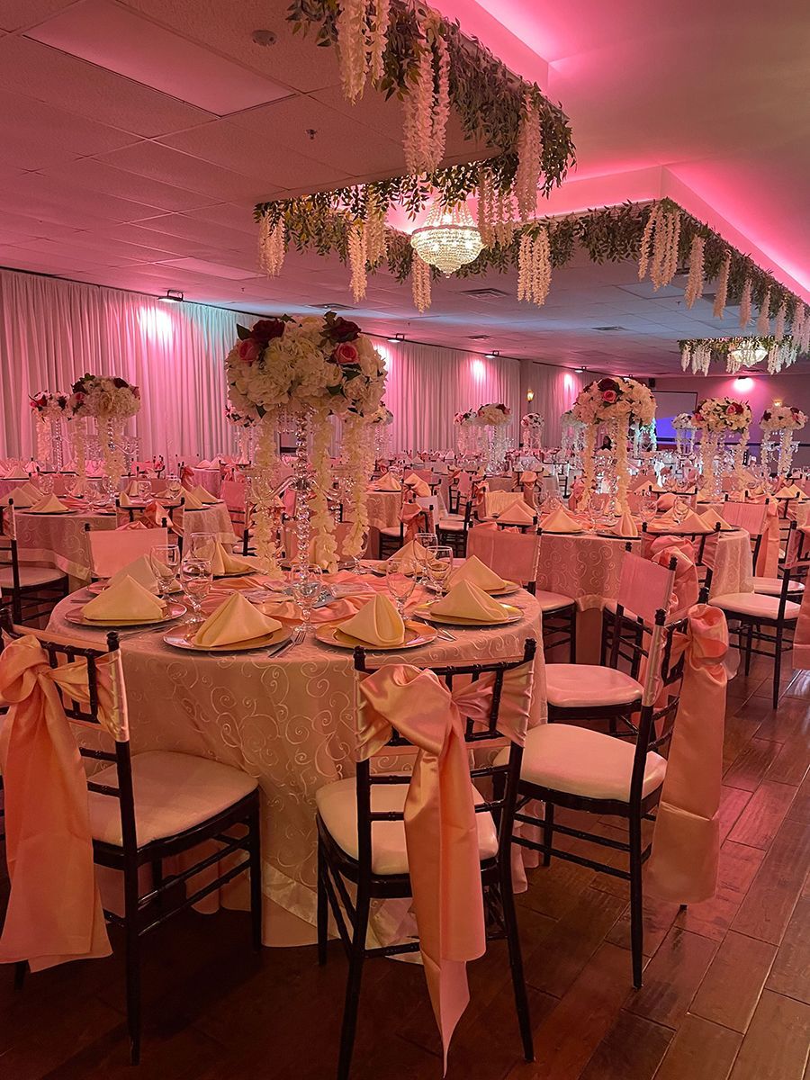 Elegant ballroom decorated with pink accents and floral centerpieces; tables set for a formal event.