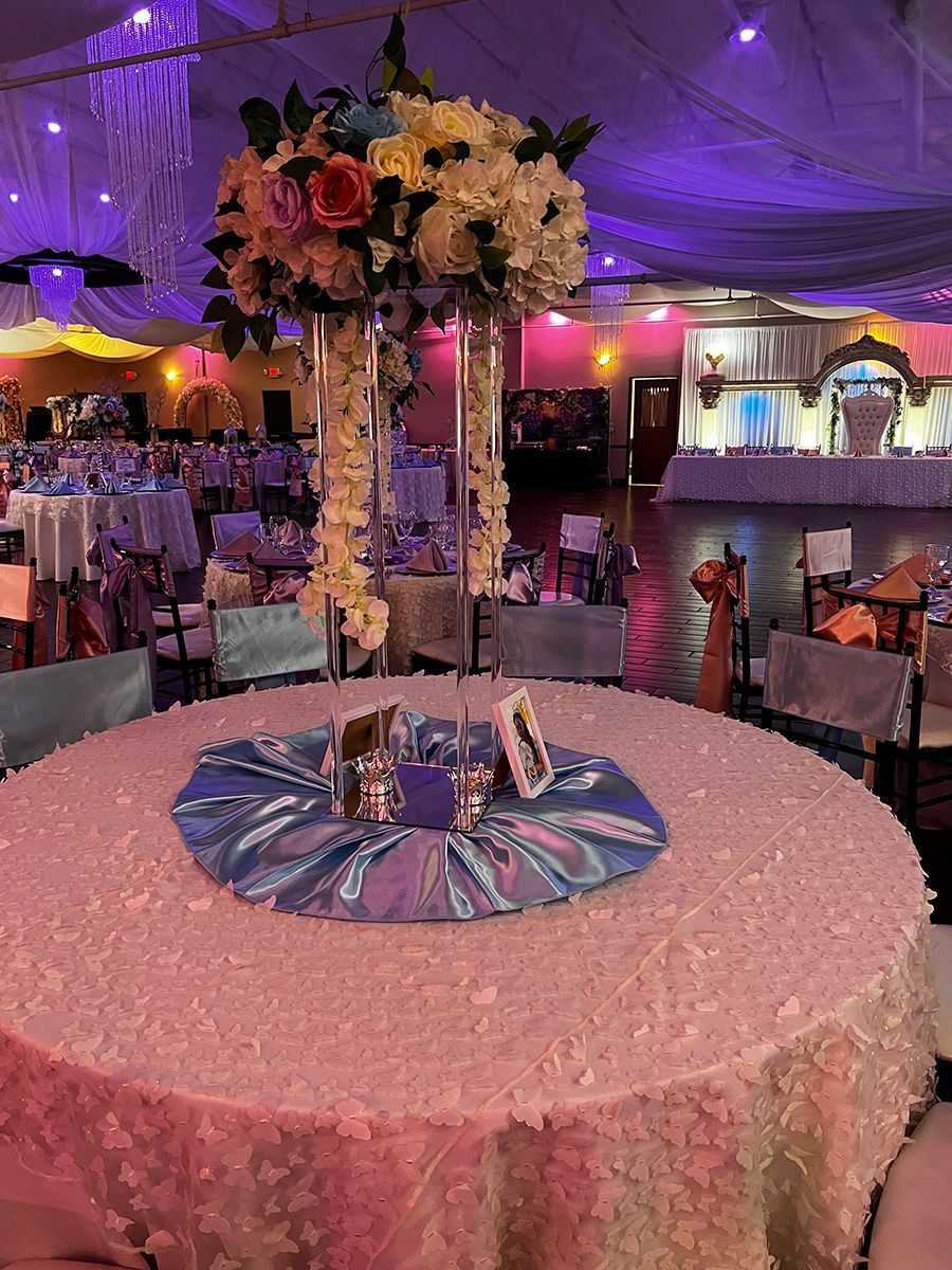 Round table set for event, with floral centerpiece and blue tablecloth. Room lit in purple.