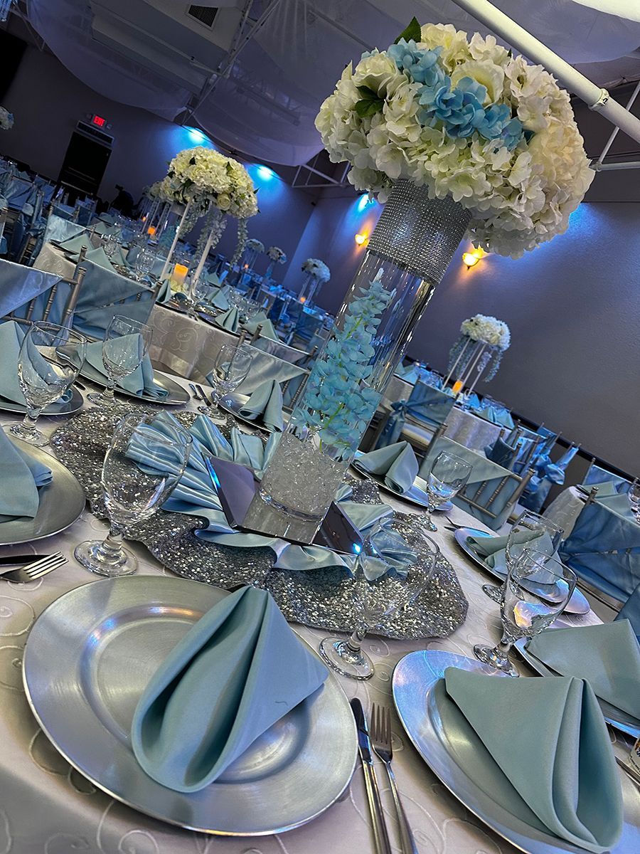 Elegant event tables set with silver chargers, blue napkins, and floral centerpieces.