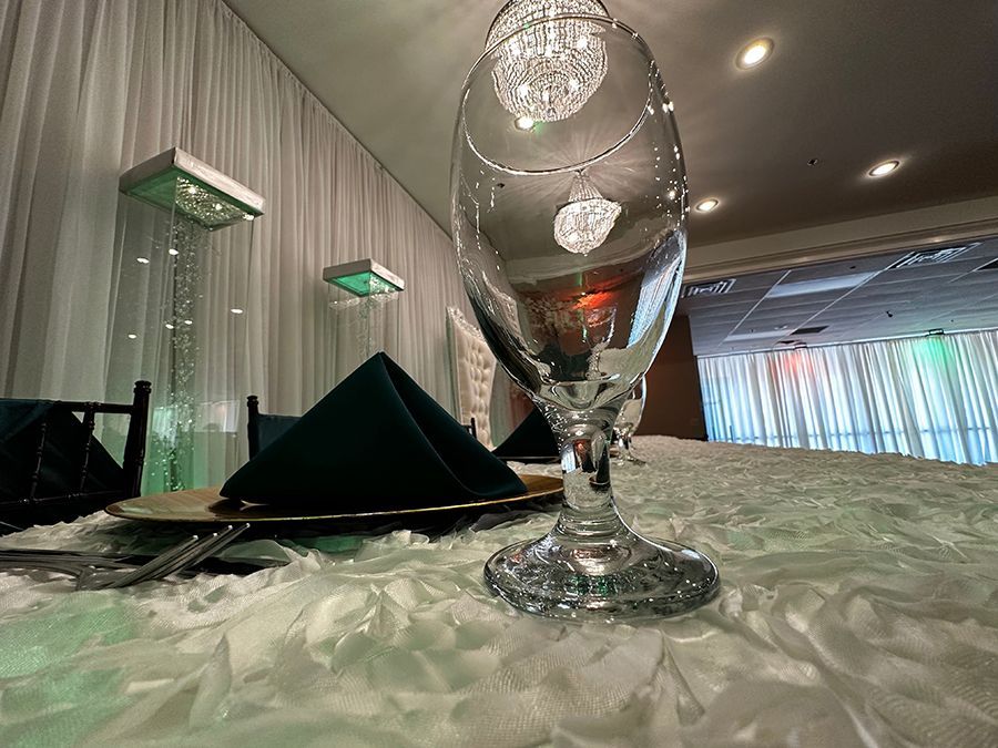 Elegant event table setting with large glass, green napkin, and crystal chandelier.