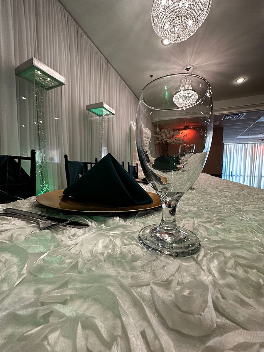 A formal dining table set for an event, with a water glass, napkin, and a decorative gold charger.
