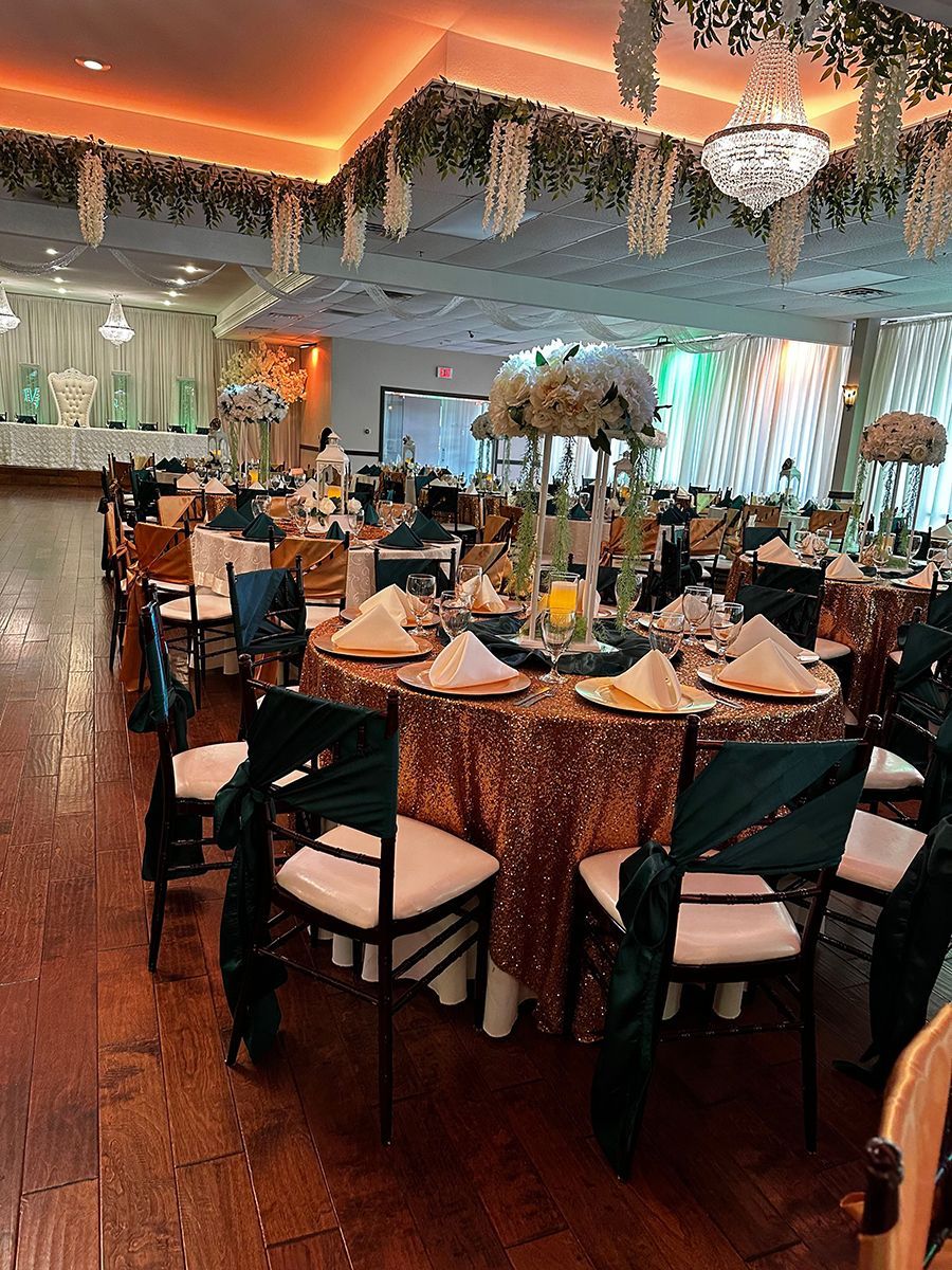 Banquet hall with tables set for a formal event; gold sequin tablecloths, teal accents, white chairs, floral centerpieces.