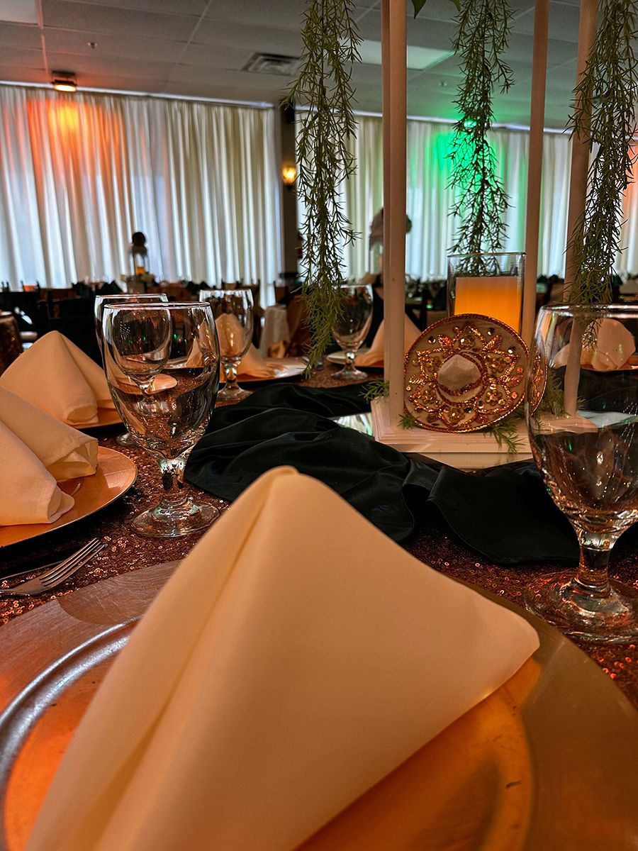 Elegant table setting with gold charger plate, folded napkin, glassware, and decorative floral centerpiece.