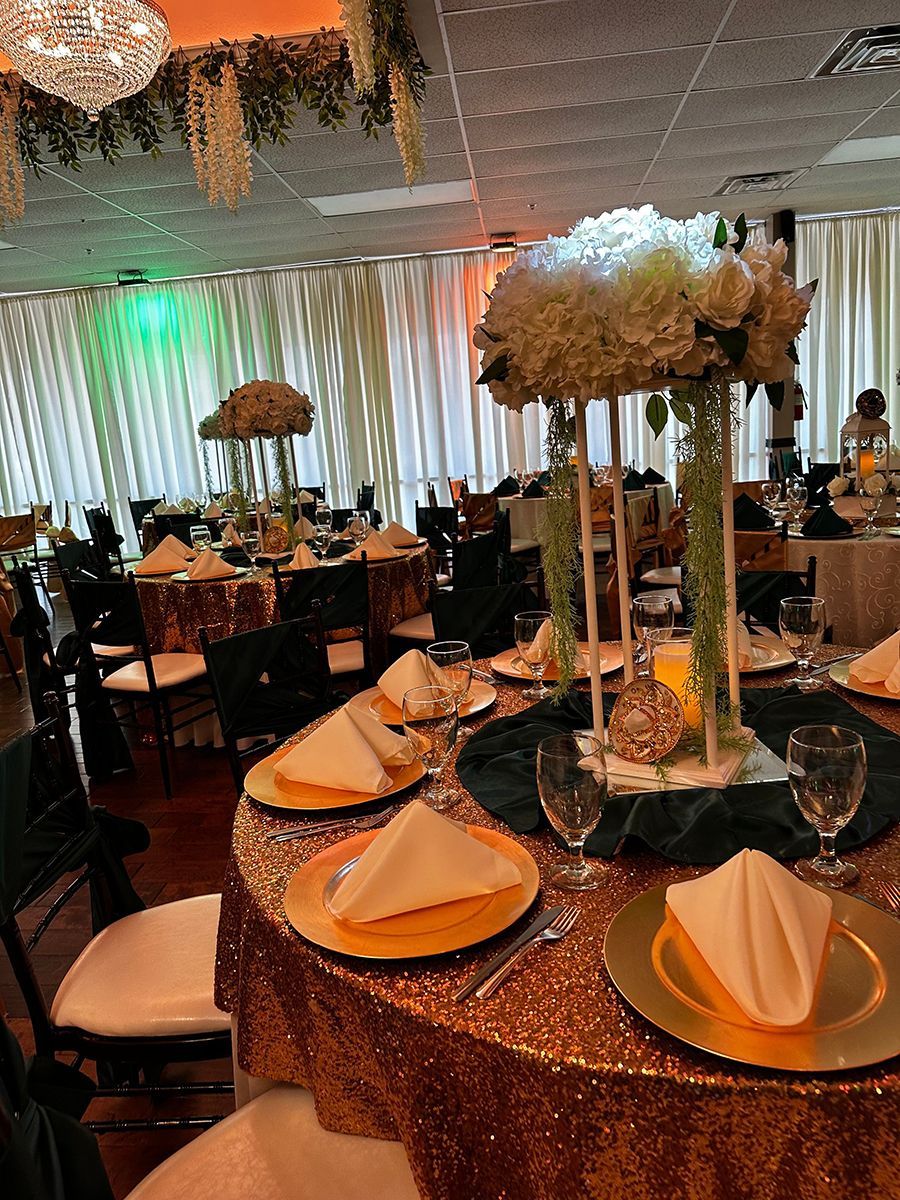 Elegant event hall with tables set for a celebration. Gold sequin tablecloths, tall floral centerpieces, and white napkins.