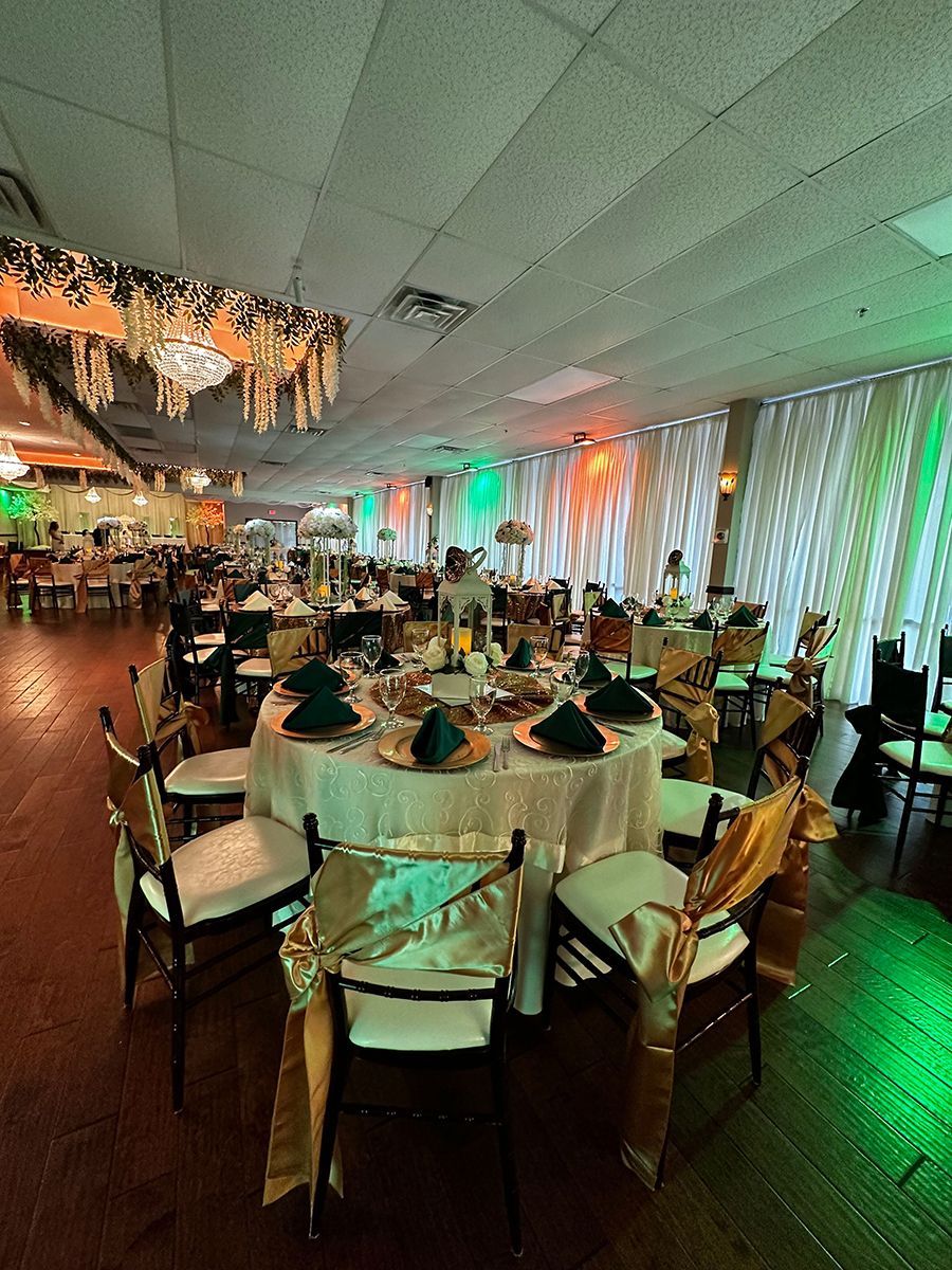Elegant ballroom set for an event; round tables with gold and green accents, and draped chairs.