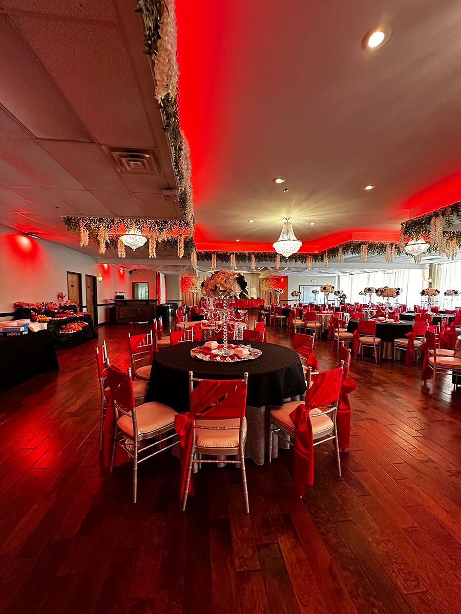 Banquet hall with tables, chairs, dark tablecloths, and red lighting.