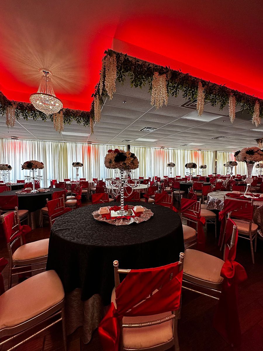 Elegant banquet hall with round tables, black tablecloths, red lighting, and floral centerpieces.