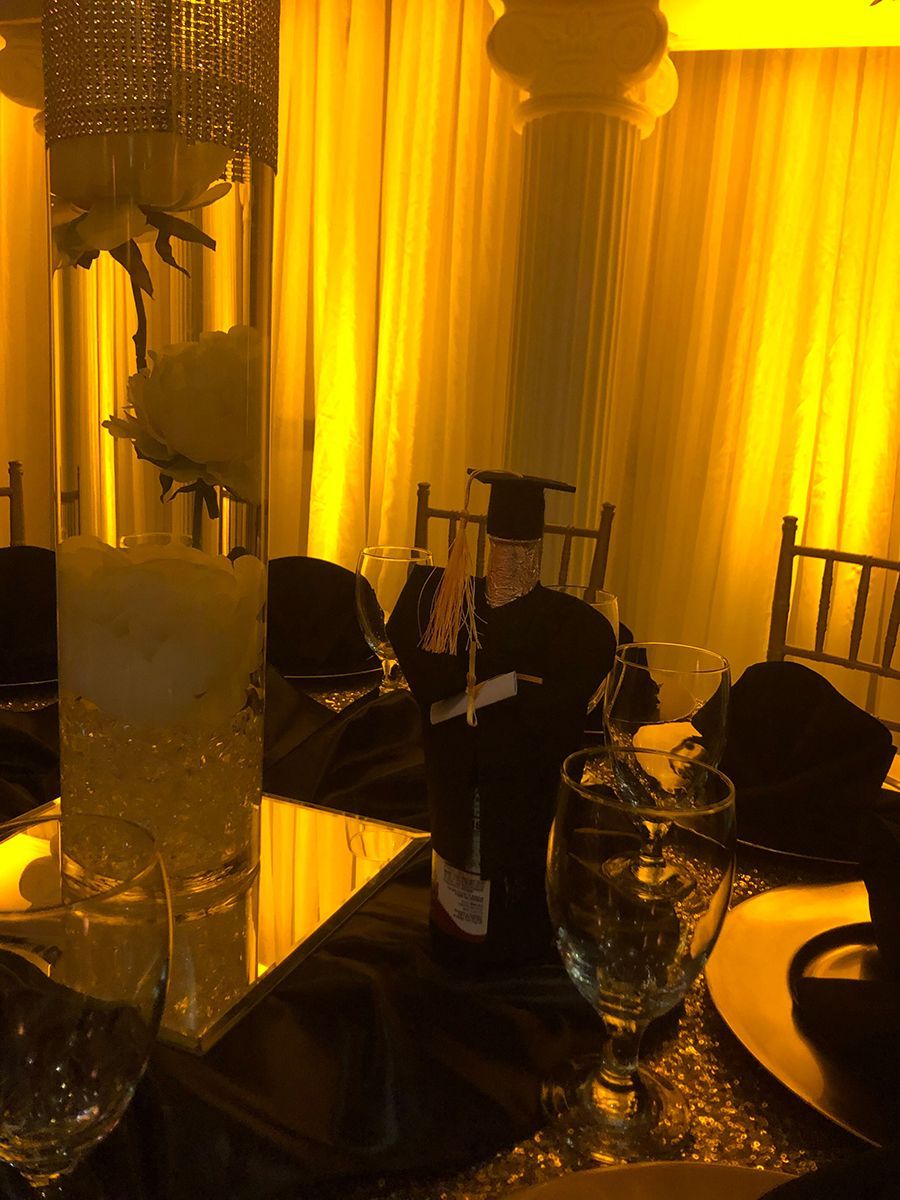 Elegant event table with floral centerpiece, yellow lighting, black tablecloth, and glasses.