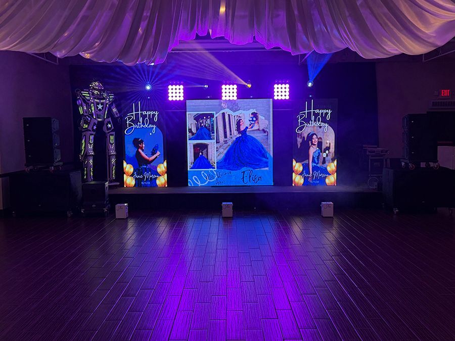 Stage setup for a quinceañera with a photo backdrop, lighting, speakers, and a robot.