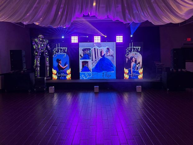 Stage setup for an event, featuring a large photo display, lighting, and robot figures. Purple lighting illuminates the scene.