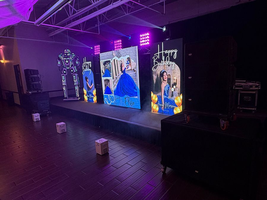 Stage setup for an event, featuring LED screens with images, purple lighting, and a DJ booth.
