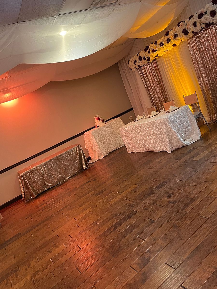 Tables with sparkly tablecloths in a decorated venue with a wooden floor.