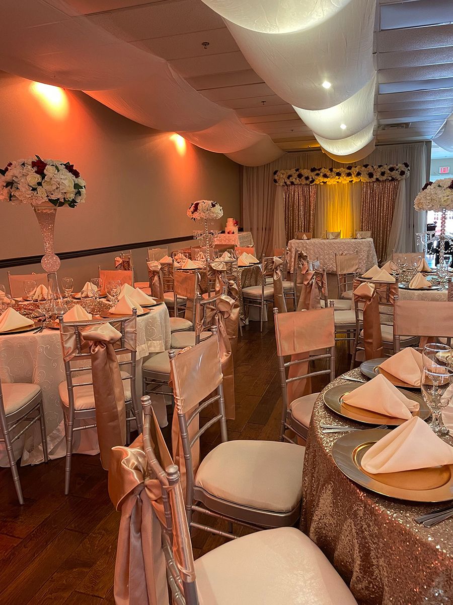 Elegant banquet hall, tables set for a formal event. Rose gold accents, floral centerpieces, and decorative ceiling.