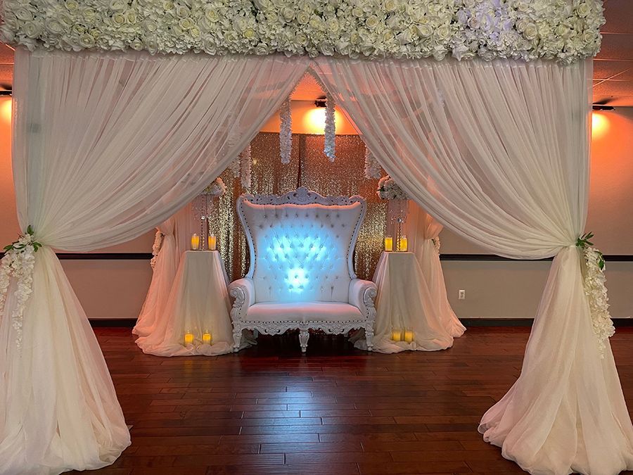 A decorated white throne setup with floral accents and draped fabric for a special event.