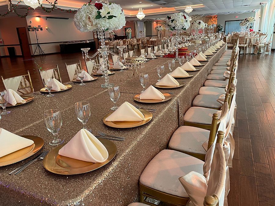 Long banquet table set for a formal event with gold accents and floral centerpieces.