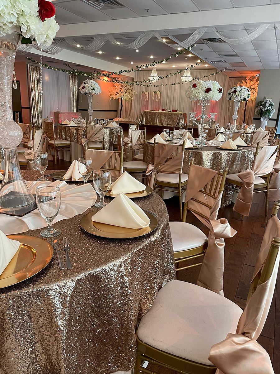 Elegant ballroom setup with gold sequin tablecloths, floral centerpieces, and decorated chairs.