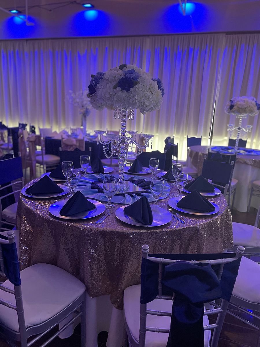 Elegant banquet table setting with blue and gold color scheme, floral centerpiece, and seated chairs.