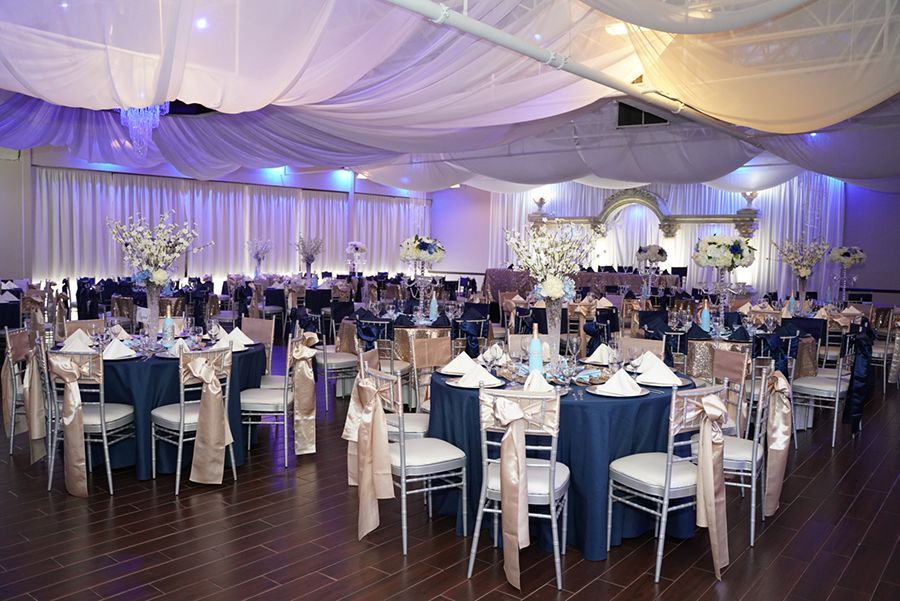 Banquet hall with tables set for a formal event, featuring navy and gold decor, and white fabric ceiling draping.