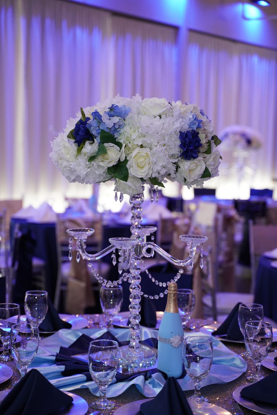 Elegant table setting with blue and white floral centerpiece, crystal candelabra, and champagne bottle.