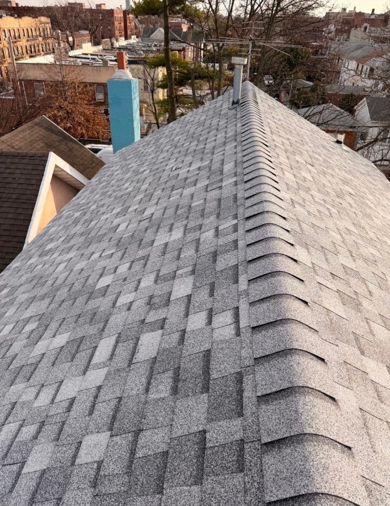 A high-angle view of a newly shingled gray roof with a prominent ridgeline, overlooking a residential neighborhood.
