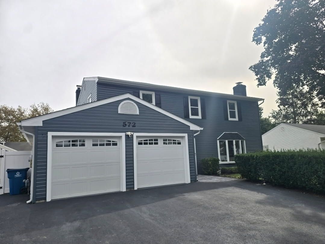 A two-story blue house with a two-car garage and light-colored doors on an asphalt driveway.