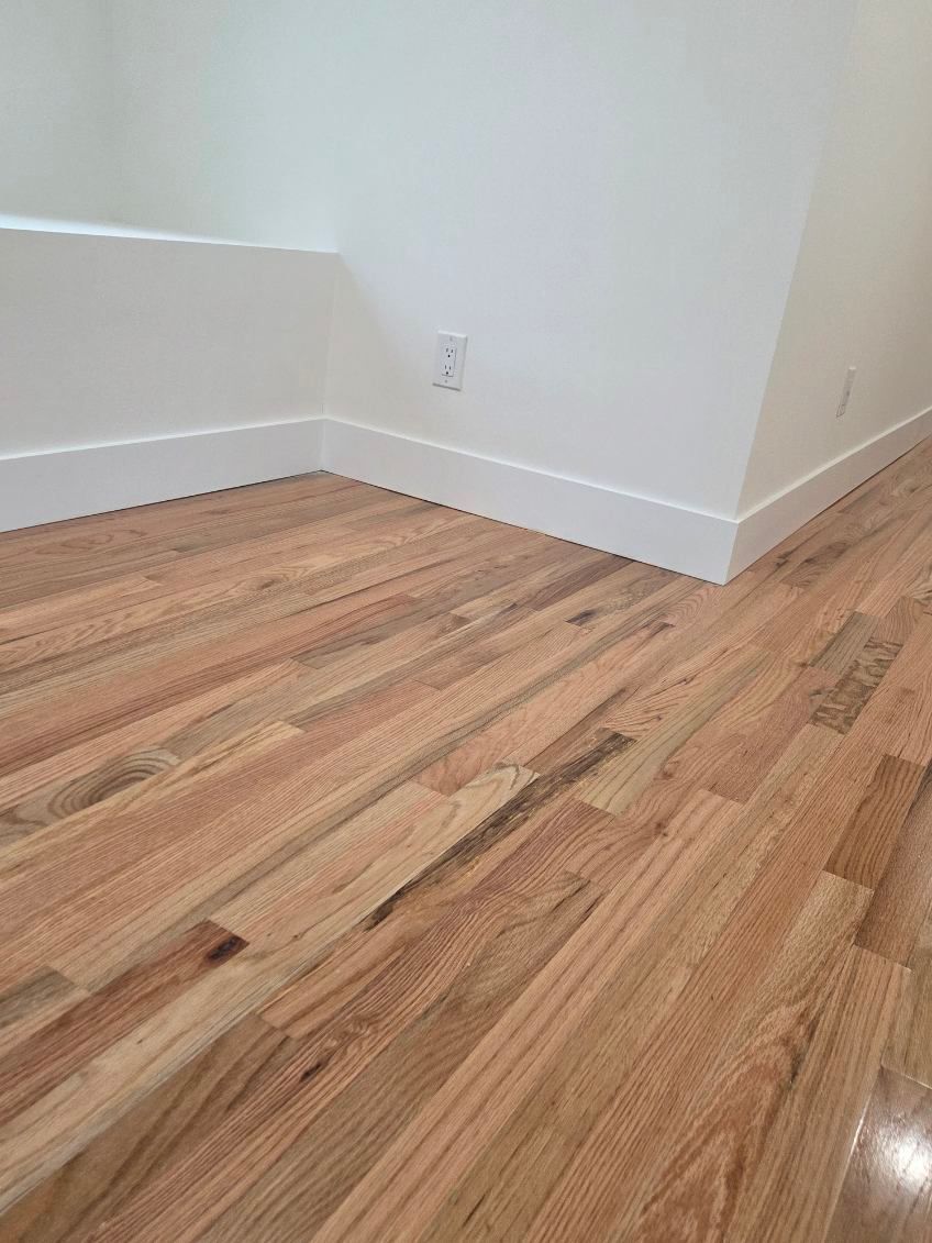 Close-up of light-toned hardwood flooring meeting white baseboards and walls in a corner of a room.